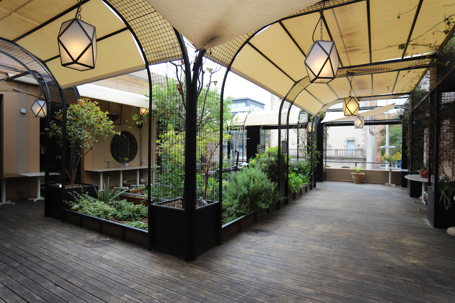 Salón de fiestas Bali en Barcelona - Terraza cubierta con arcos de hierro forjado, farolillos y jardín central con vegetación